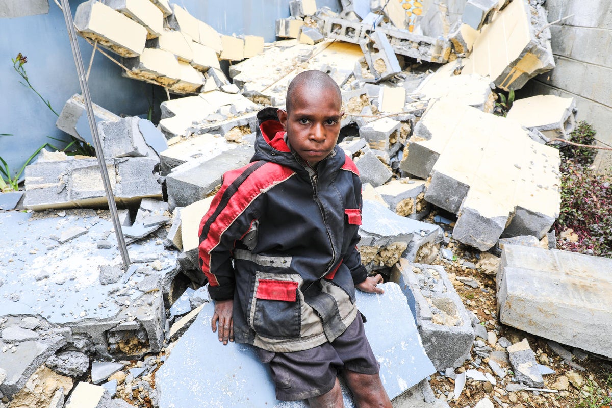 A boy is seating on a pile of rubble.