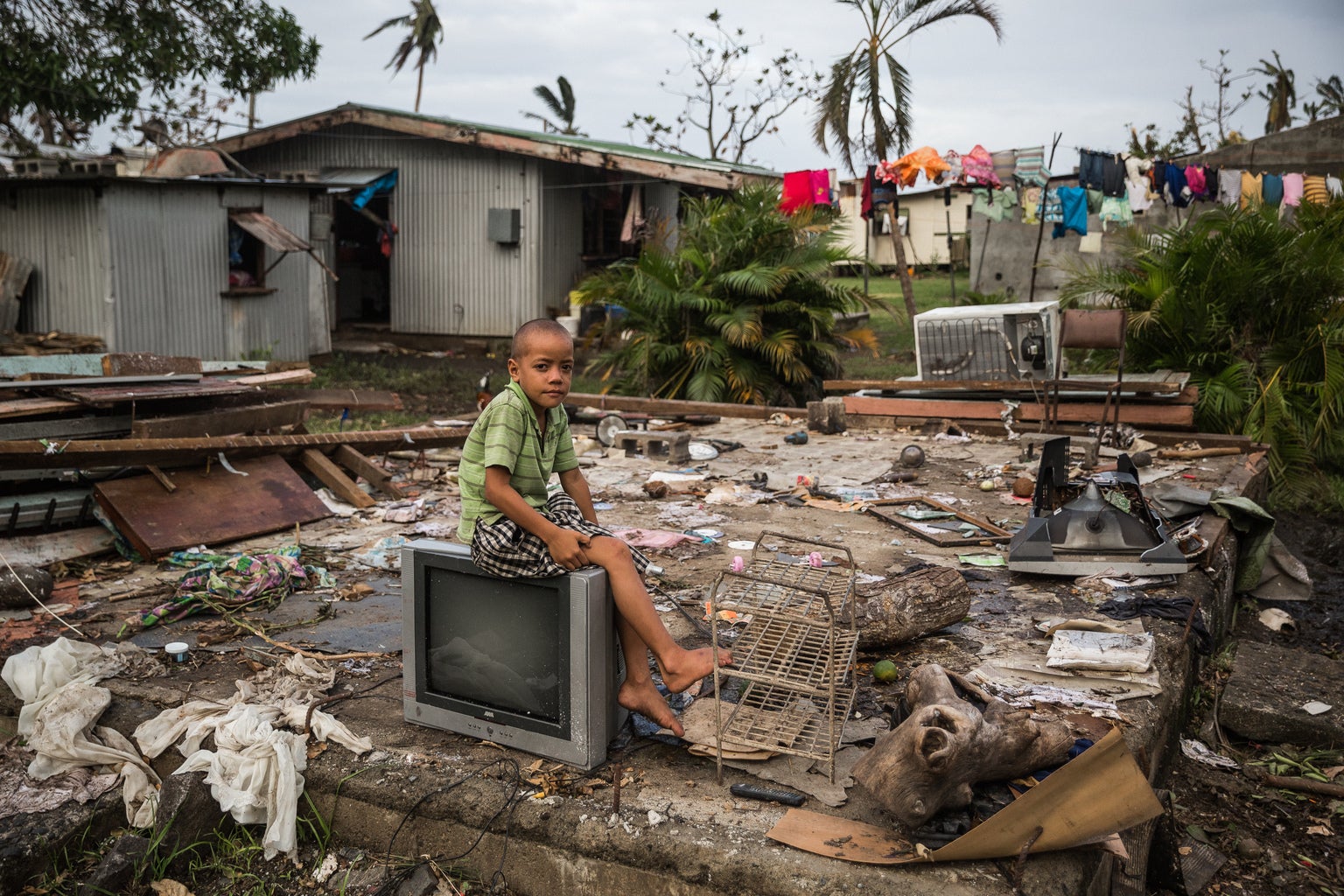 A boy is seating on a broken TV, surrounded by rubble