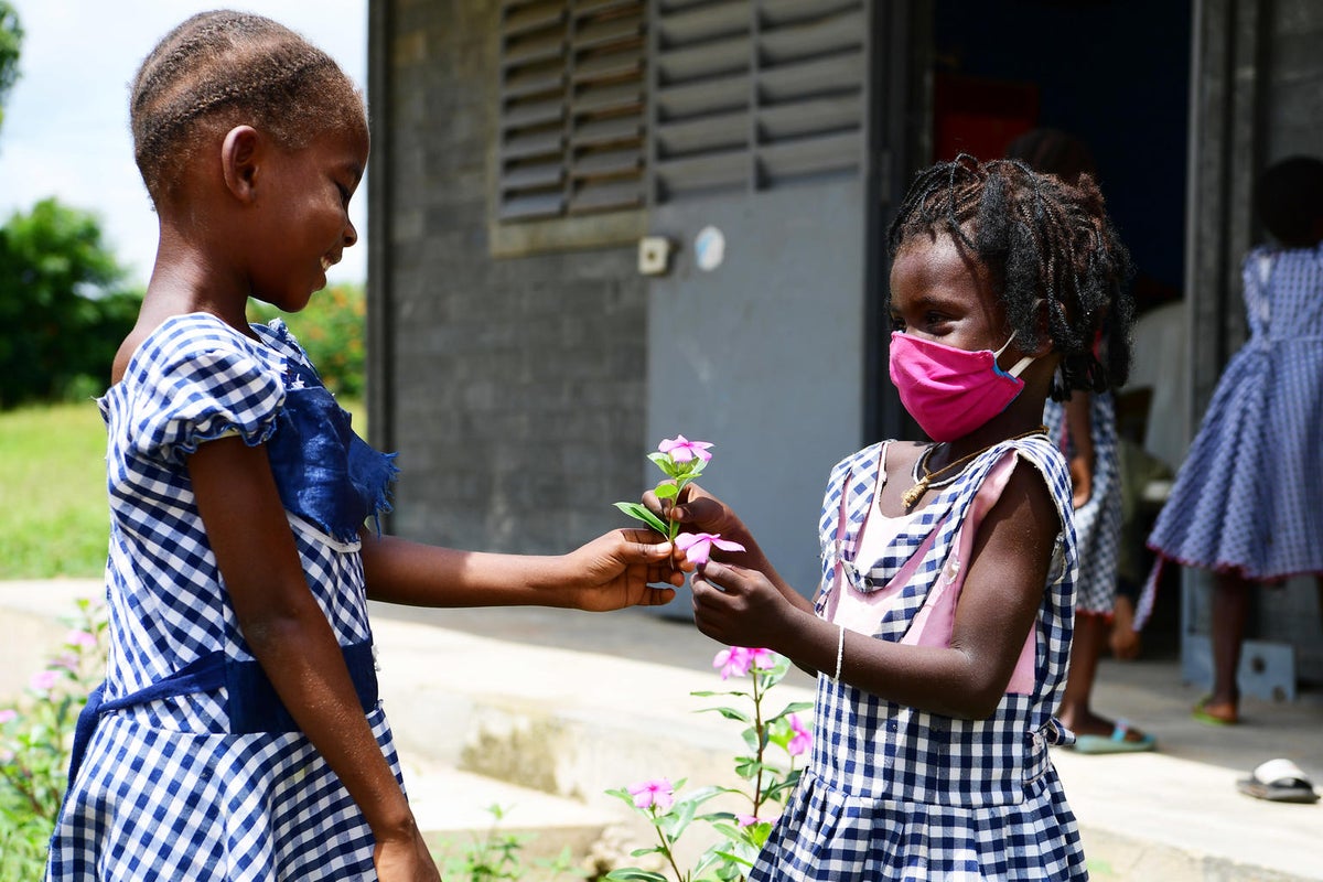 One girl is offering a flower to another girl. They are both wearing school uniforms and are smiling.