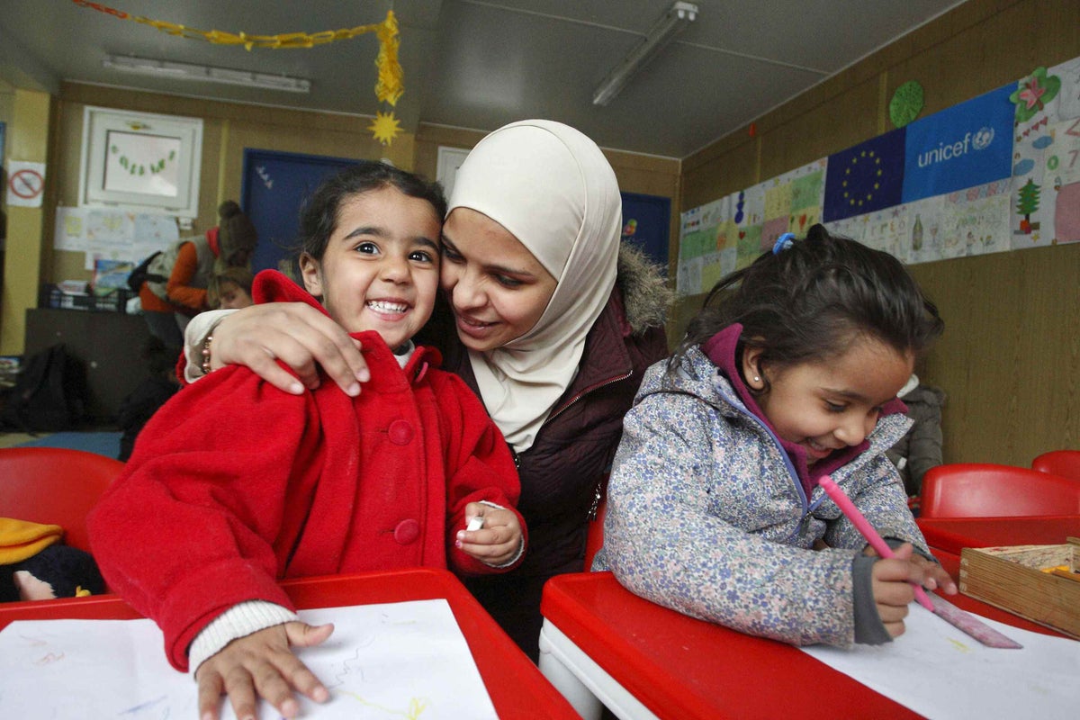 Sifar Shaabu kisses her three year-old daughter Nur, while her older daughter Lin draws in a UNICEF-supported child-friendly space in southern Serbia. 