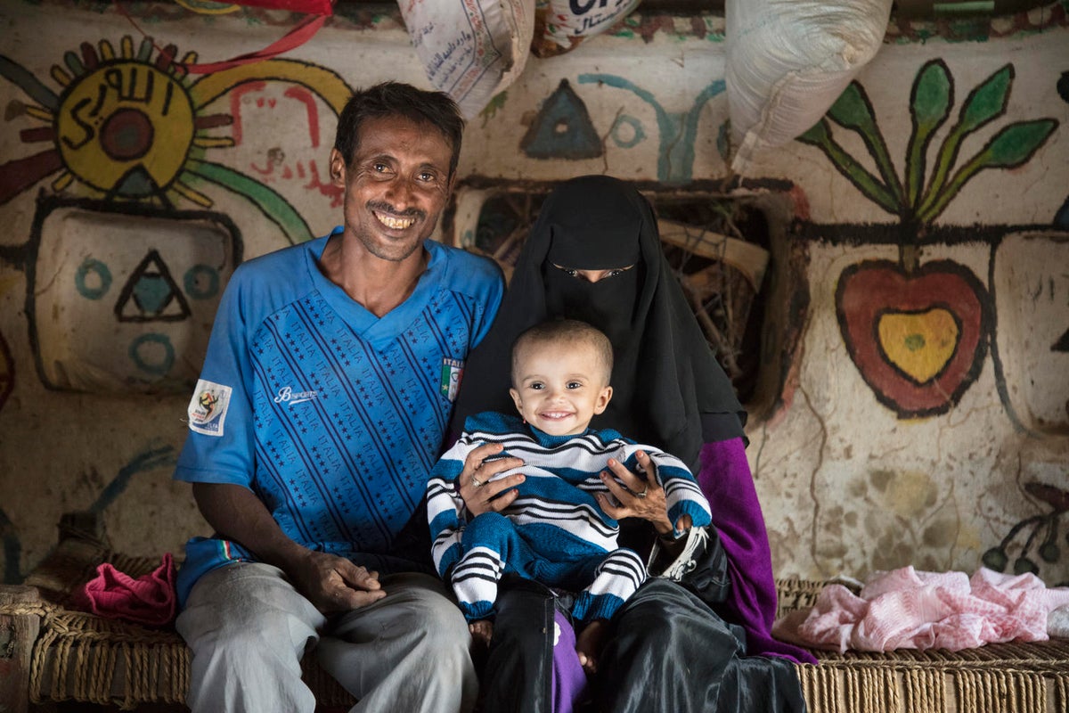 A man and a woman with a burqa looking at the camera. The woman has a baby on her lap and she looks happy.