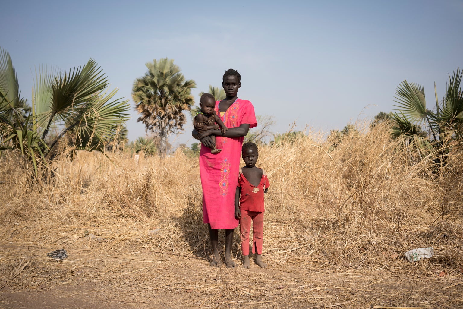 Anyang, 19, holds her one-year-old son Adhel, as her three-year-old daughter stands next to her in Apada village where they live on the outskirts of Aweil town, South Sudan
