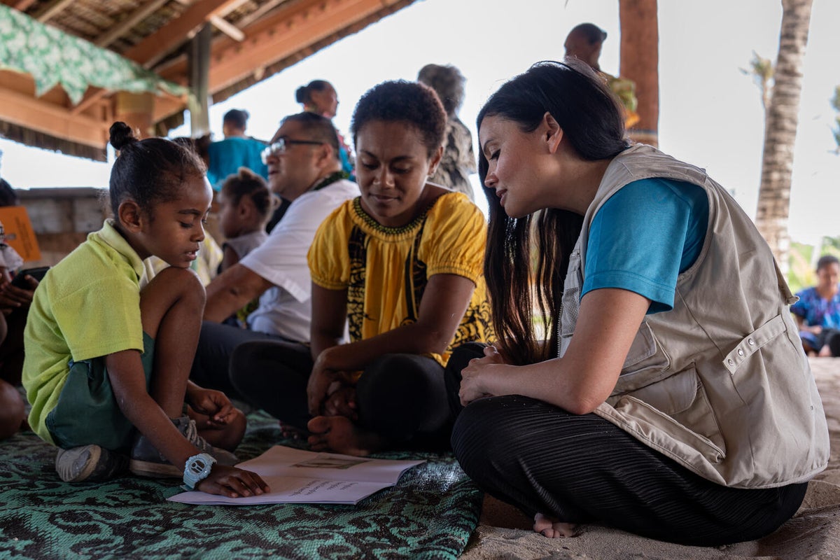 A young boy reads a story from one of his book to a UNICEF staff member