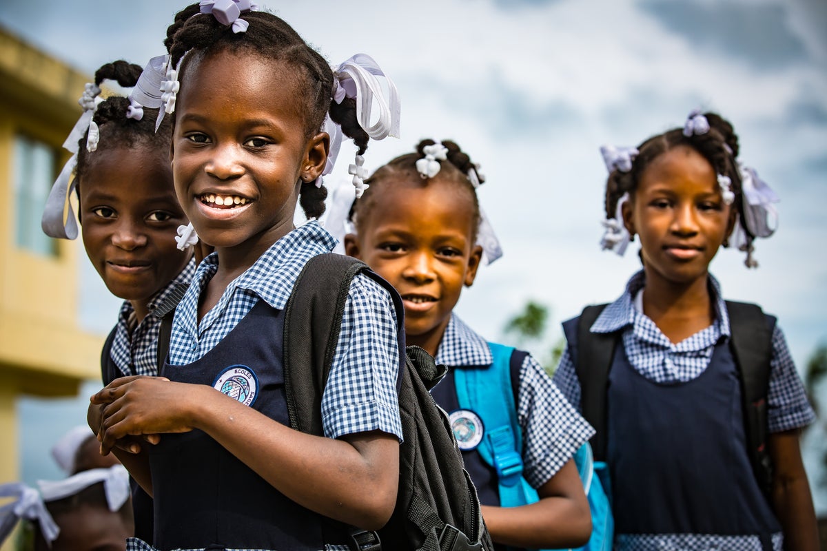 A group of four girls in their school uniforms smile to the camera.