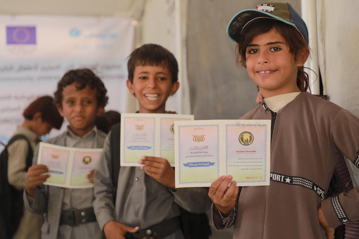 Three boys hold up their birth certificates. 