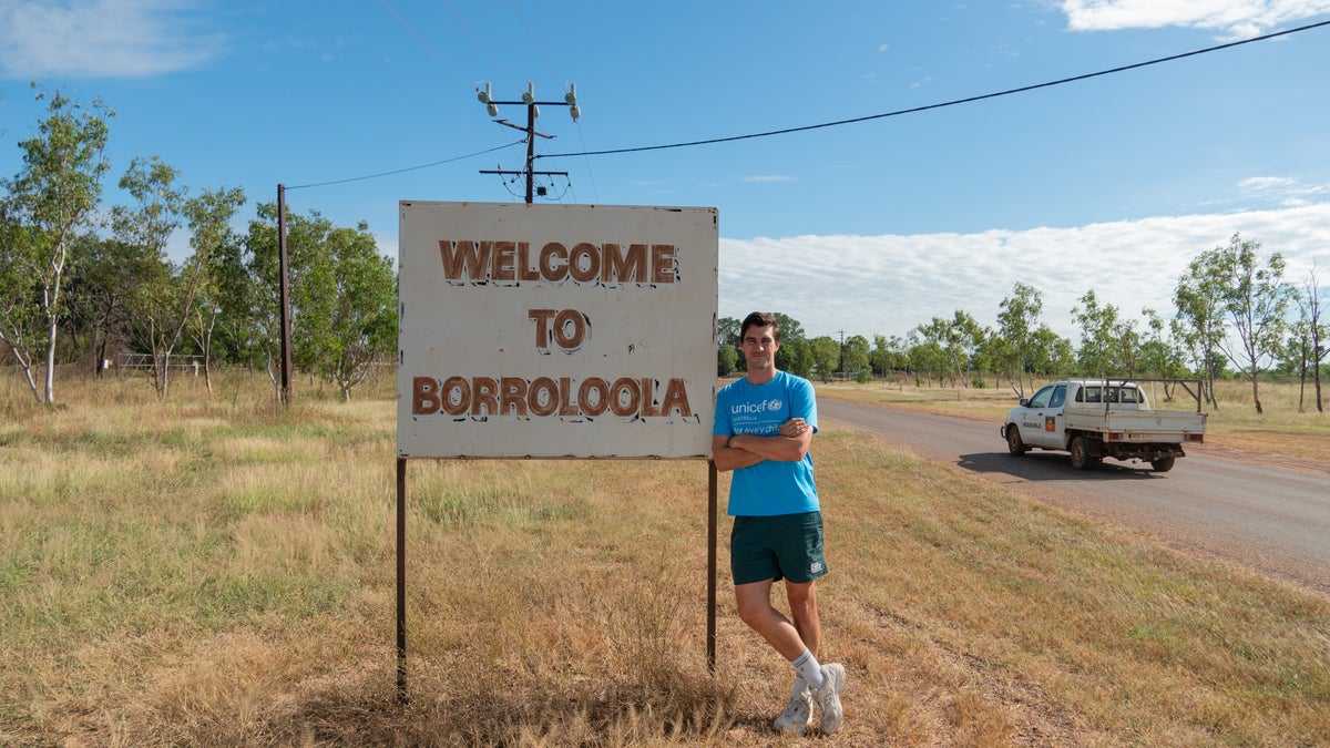 A man stands next to sign on the road. 