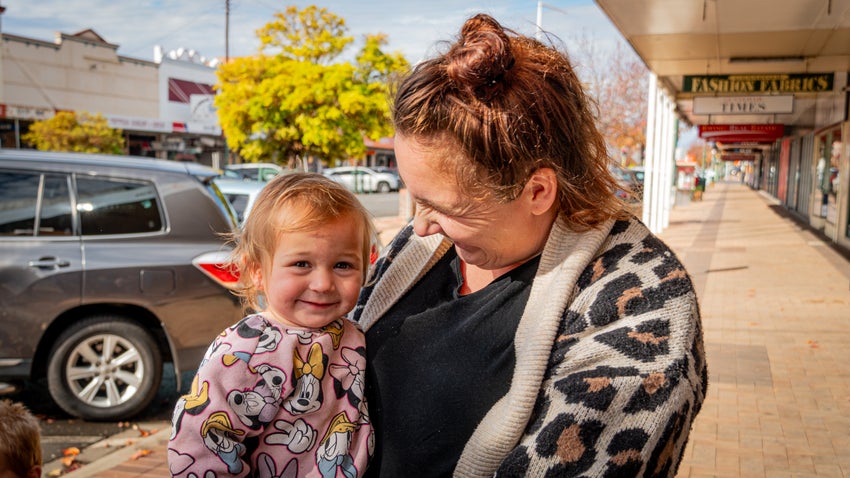 A mother smiling at her daughter as they stand on the street. 