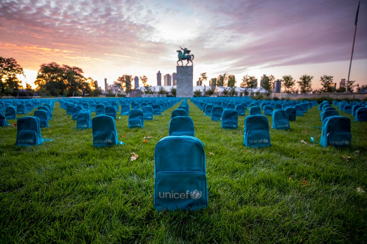 A series of UNICEF backpacks set up on a grass field as if they were graves in a cemetery