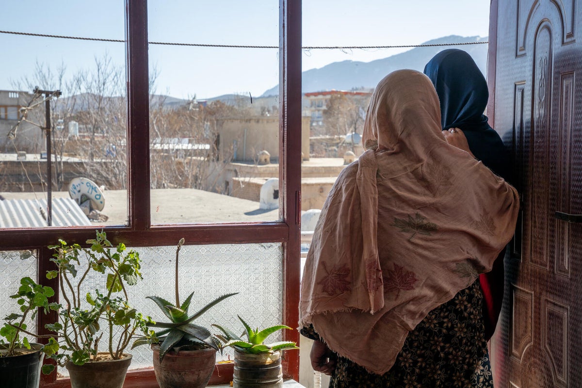 Two women gaze out the window at roof tops.