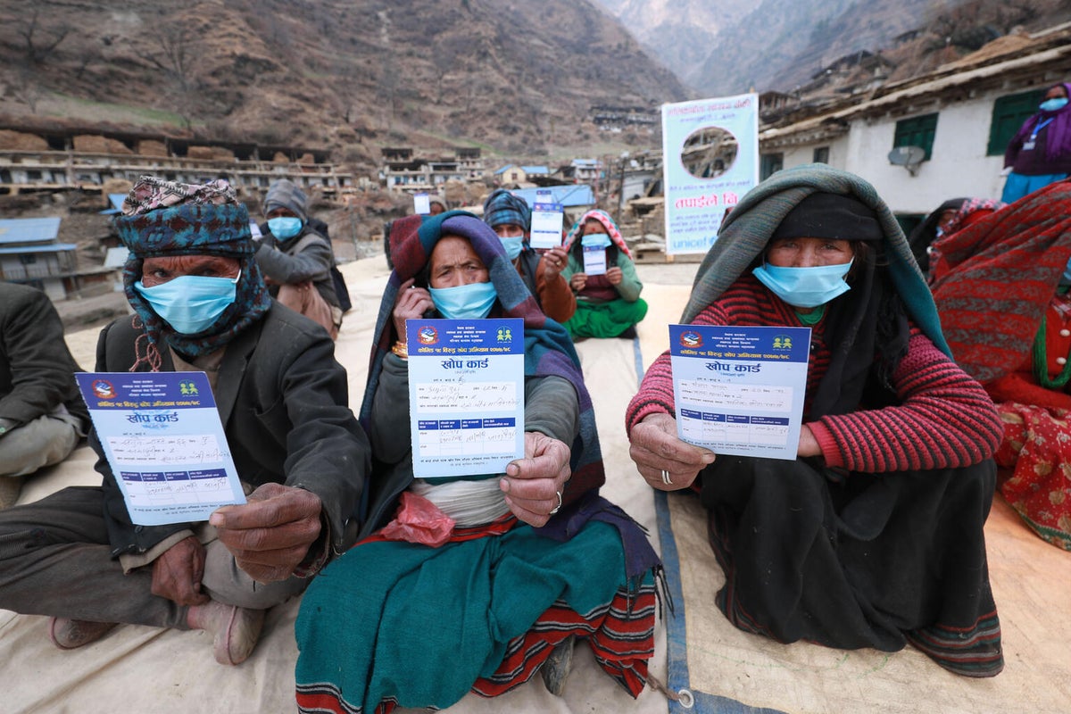 Three older women show their vaccination certificate to the camera.