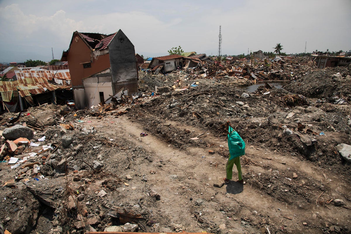 A boy carries a bag. He is walking through a land full of rubble.