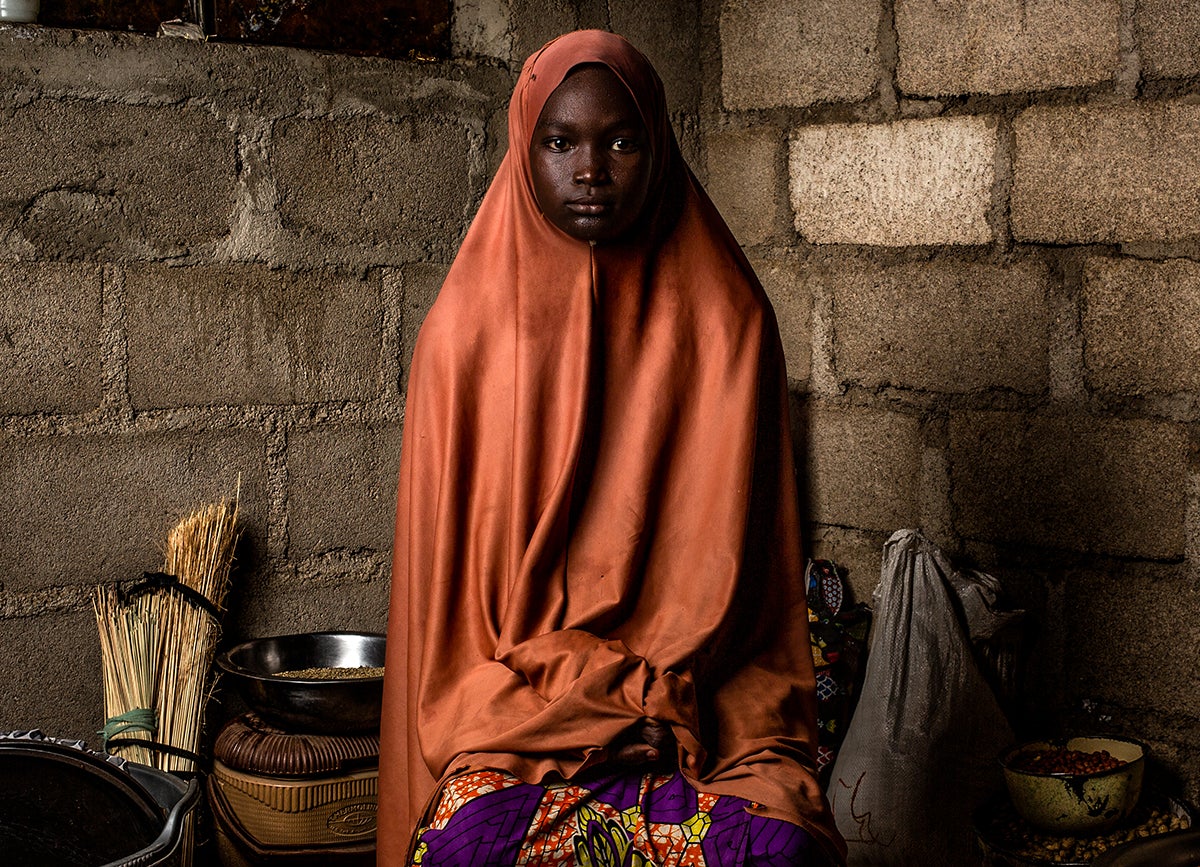 Young woman sits in her kitchen, wearing a orange shawl.