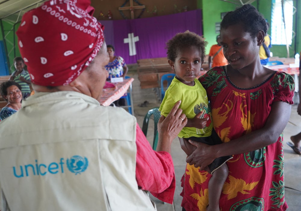 A woman carries her child next to a health officer