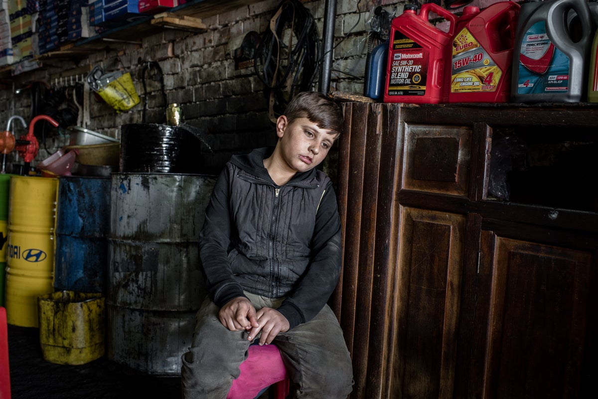 Teen boy rests against a wooden chest in a mechanic garage.