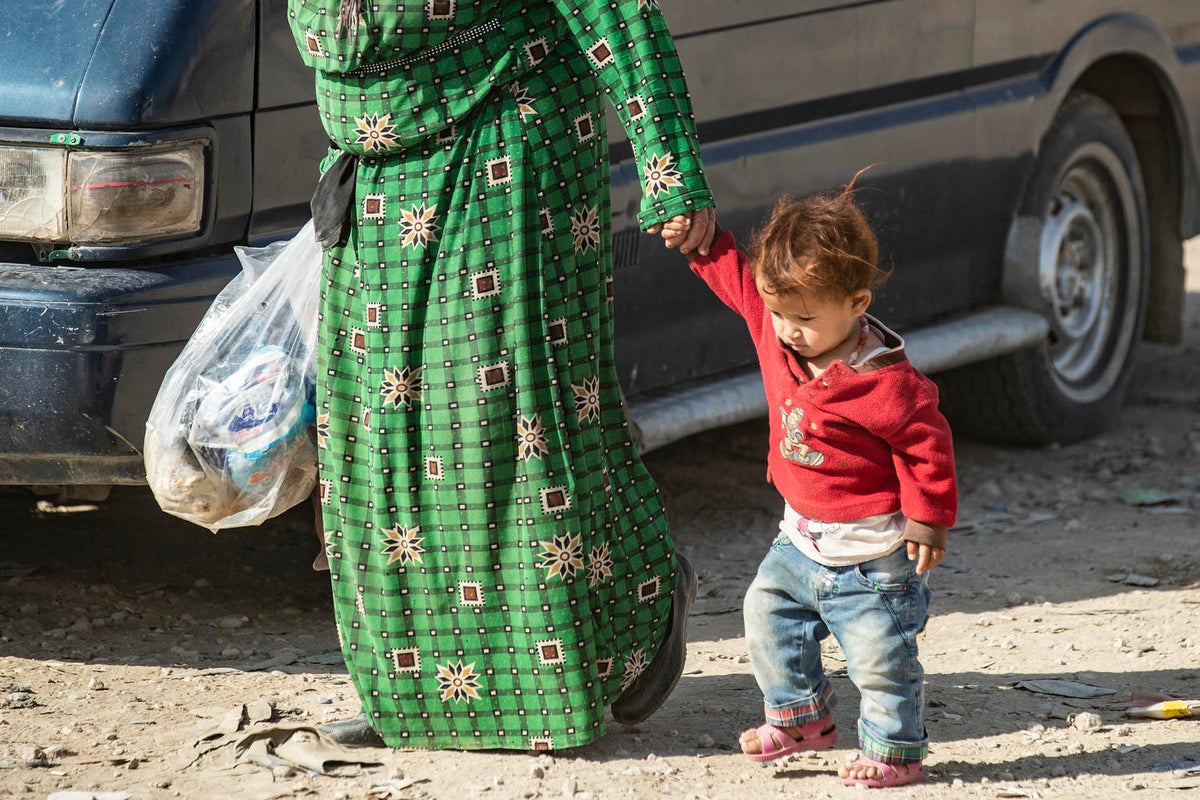 A woman is walking holding a toddler by their hand.