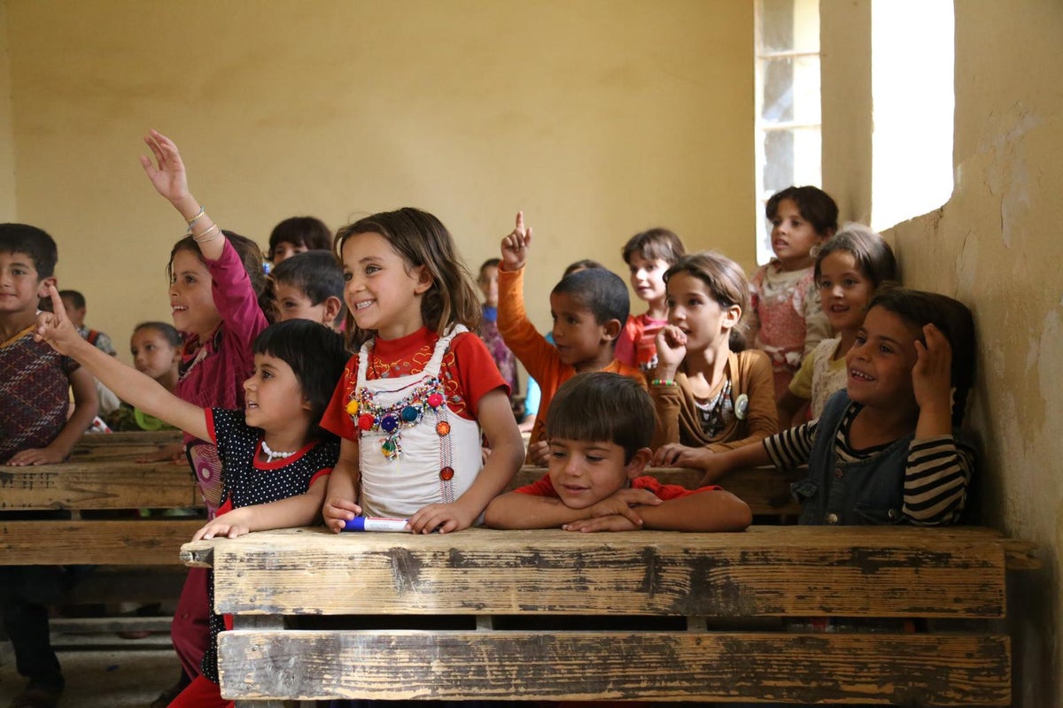 A group of children raise their hands in a classroom.