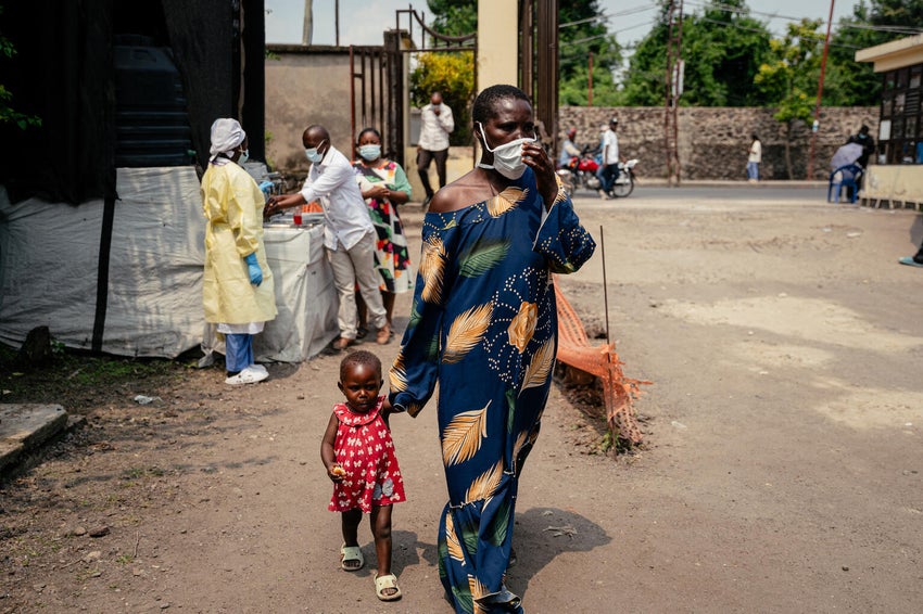 A mother, who's wearing a mask as a preventative measure, enters a hospital after passing a checkpoint for hand washing and health screening in the DRC during the 2026 Ebola outbreak.