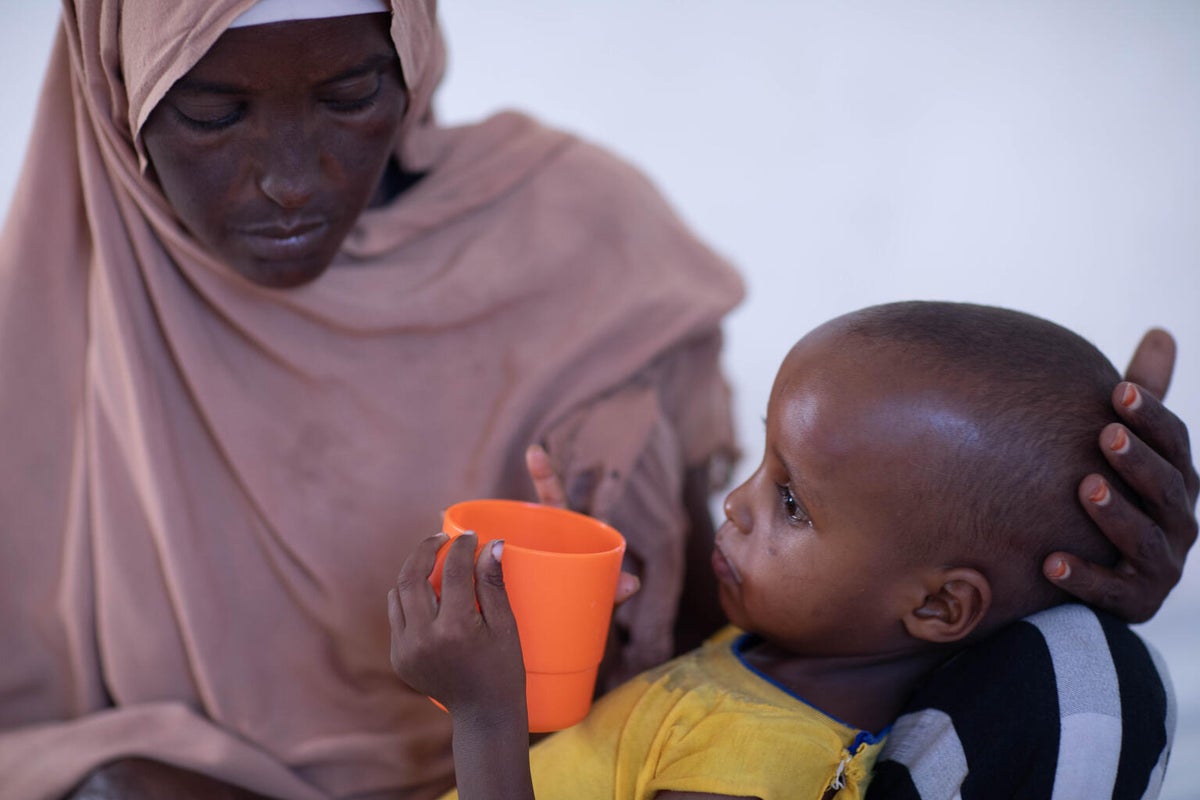 A Somalian mother holder her child as she drinks from a cup