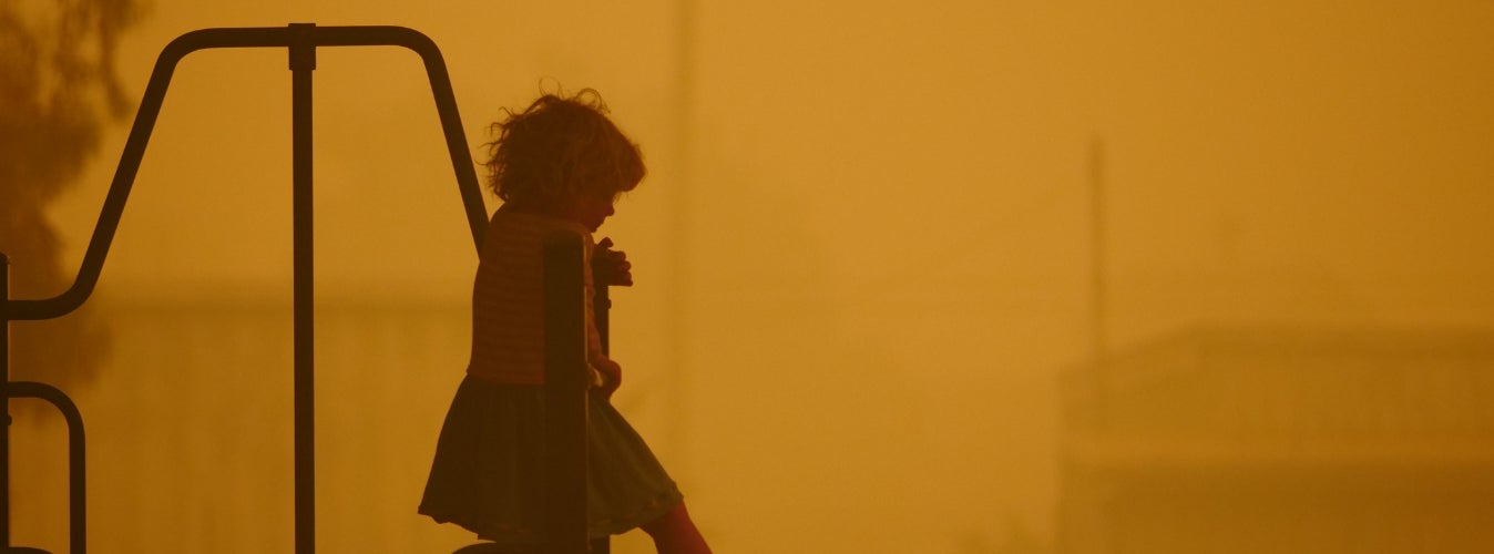 A young child standing on playground equipment against a red smoky sky. 