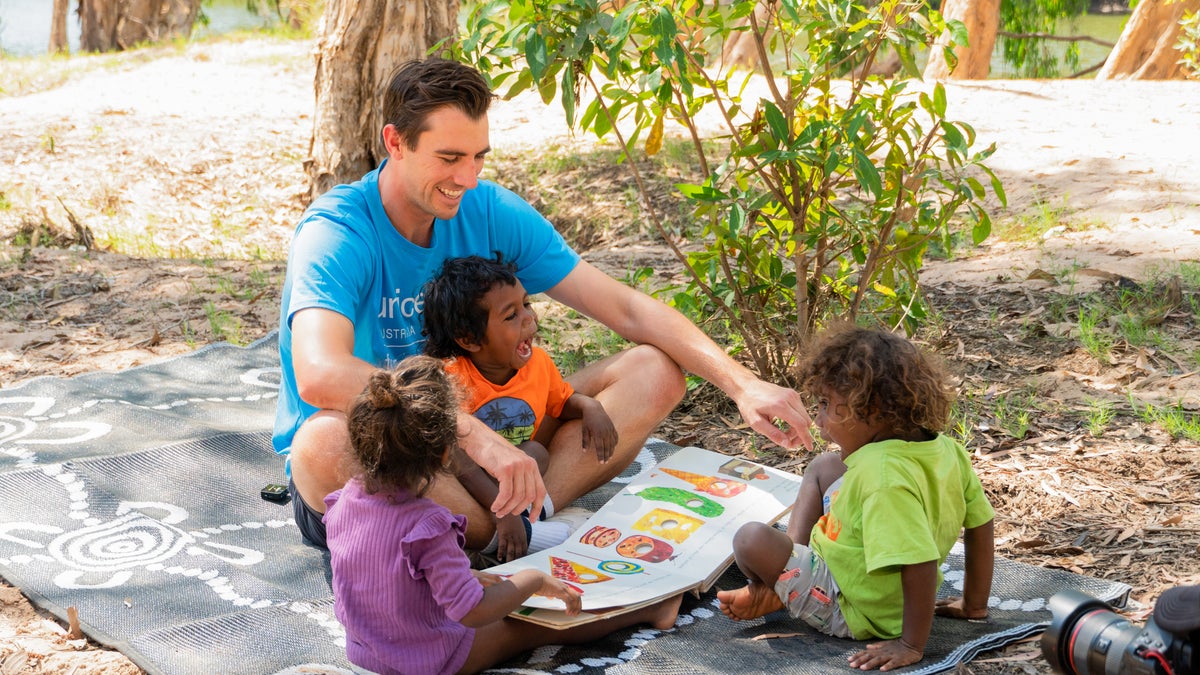 Cricketer Pat Cummins reading book to three Australian Indigenous children