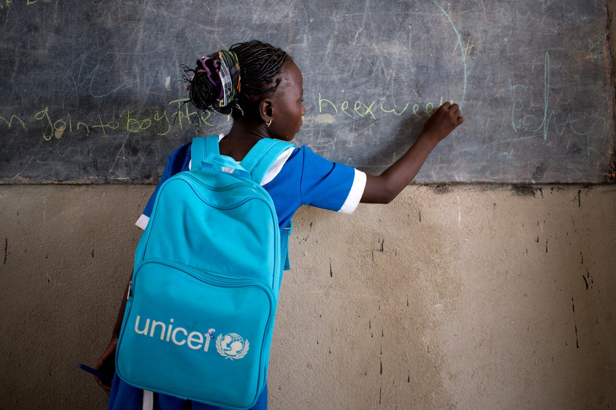 A girl is writing on a chalkboard. She is wearing a UNICEF backpack.