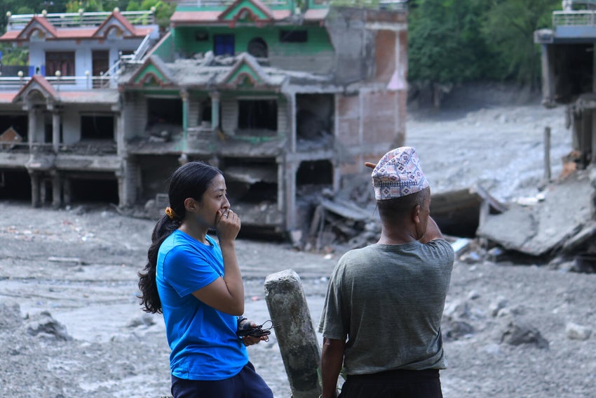 UNICEF staff talking to community members in Nuwakot District, Nepal, as homes and surrounding areas can be seen covered in mud.