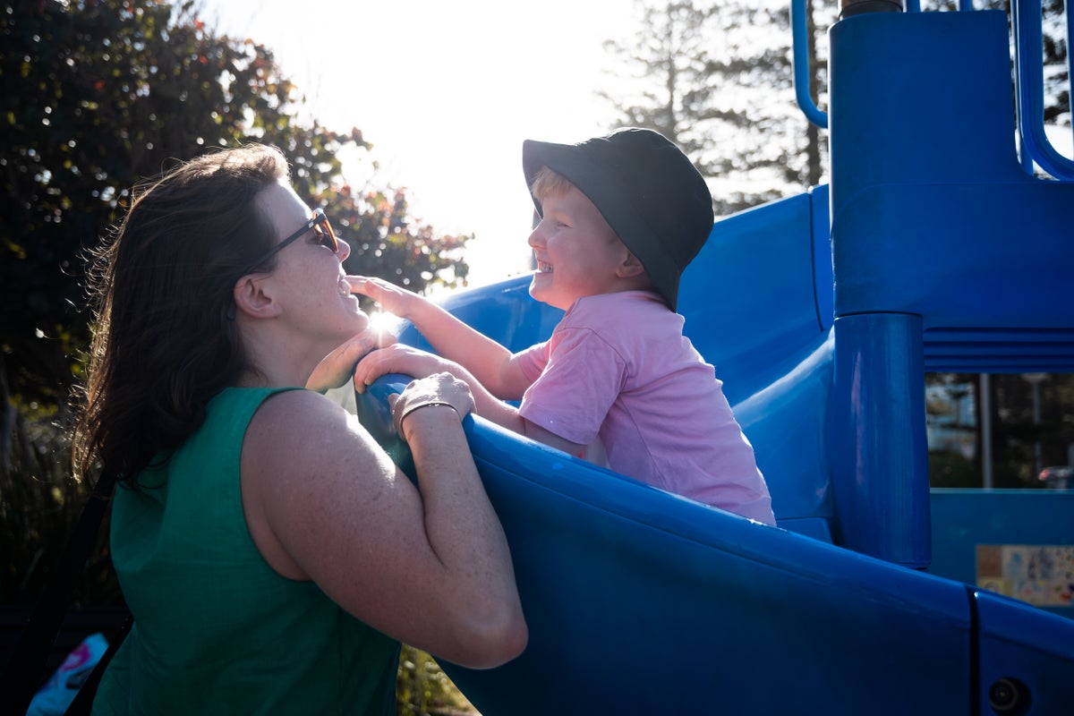 A mother and son play on a slide in a playground.