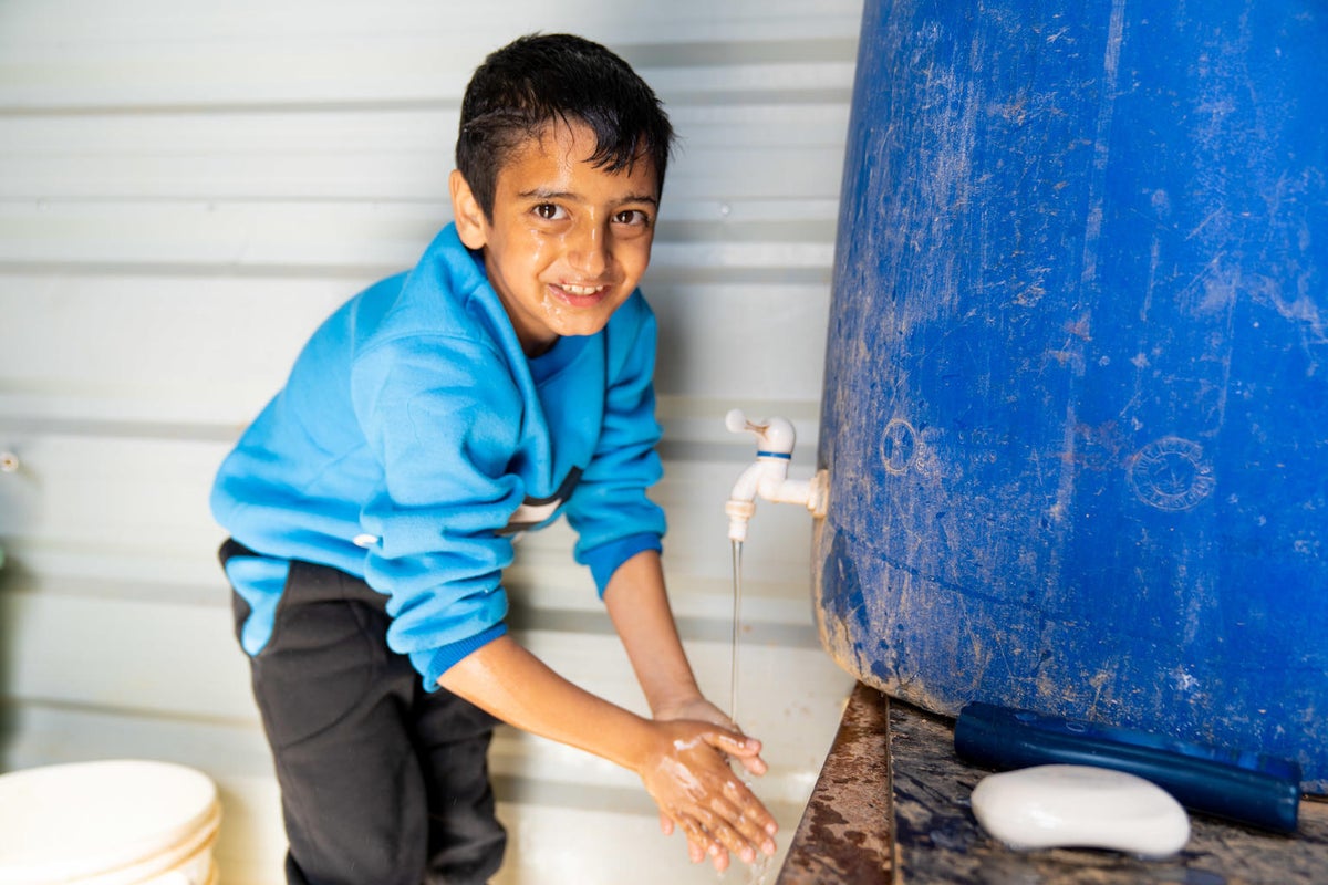 A boy is getting water from a tap that comes from a water tank.