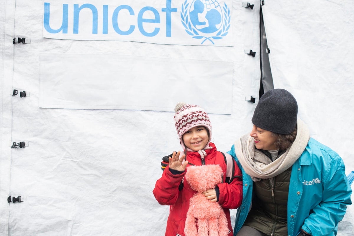 A young girl stands next to UNICEf staff