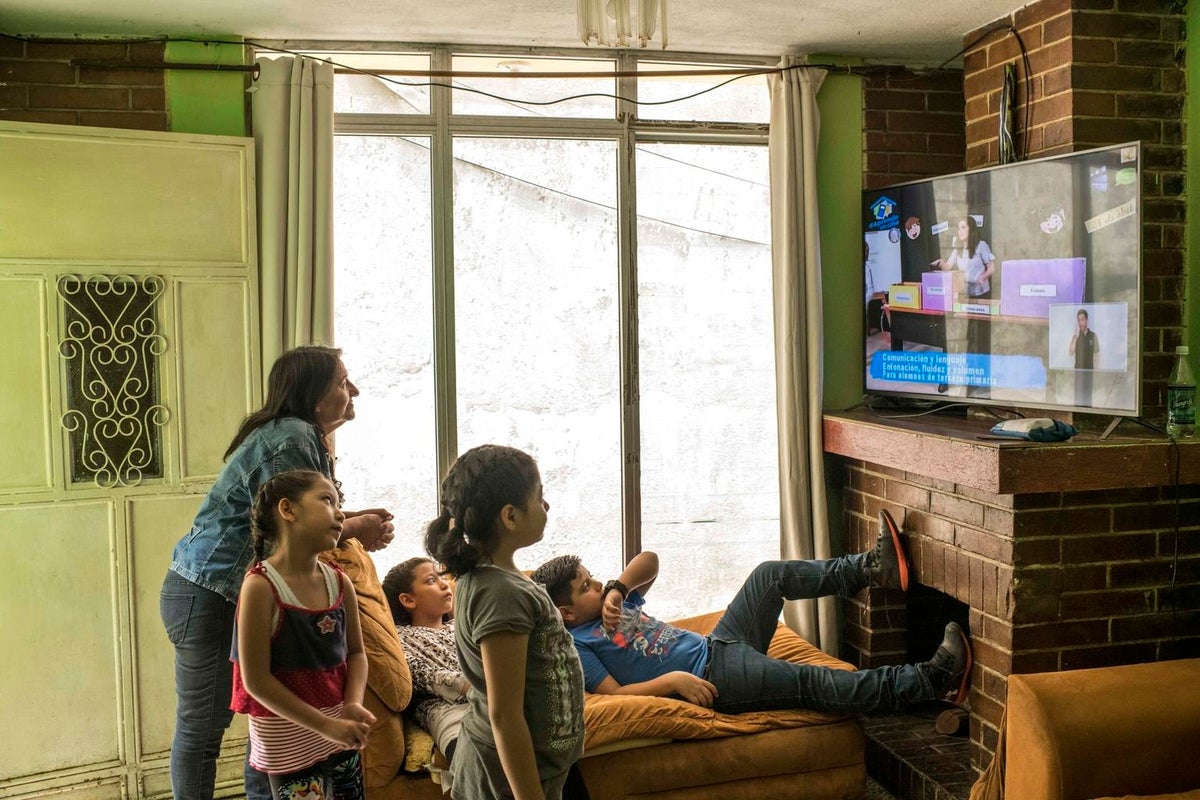 A group of four children are watching TV with a woman.