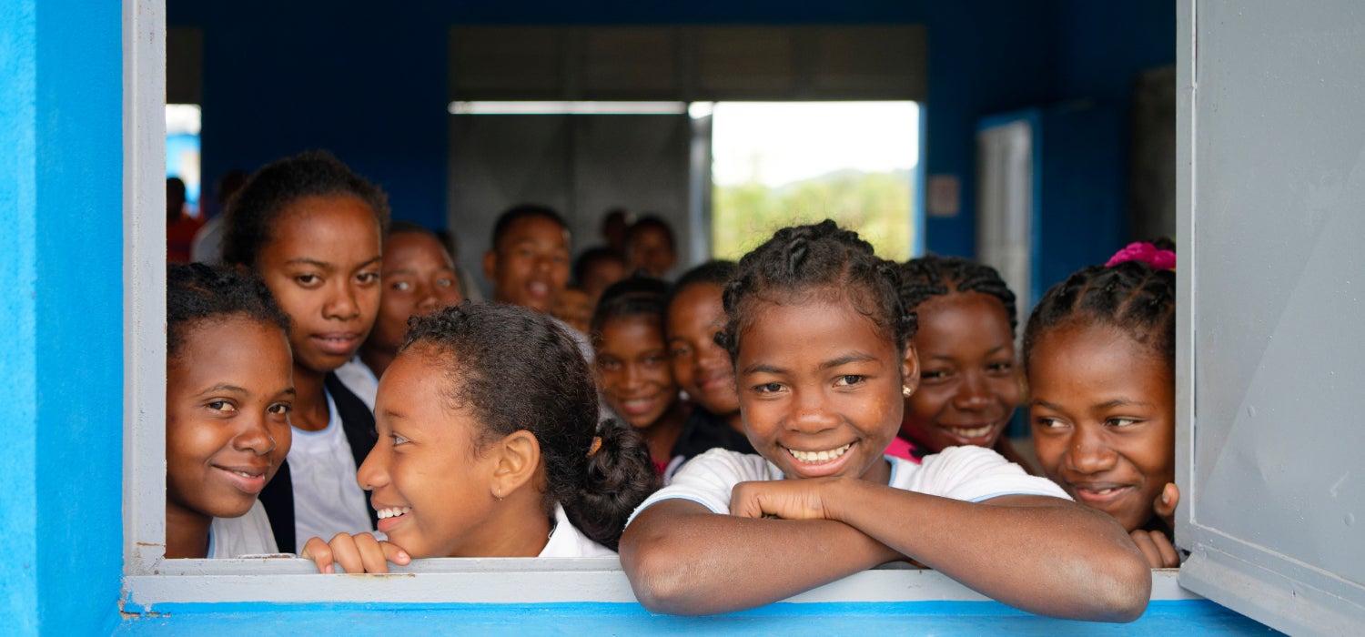 A group photo of smiling students looking through the open window of their classroom in Madagascar.