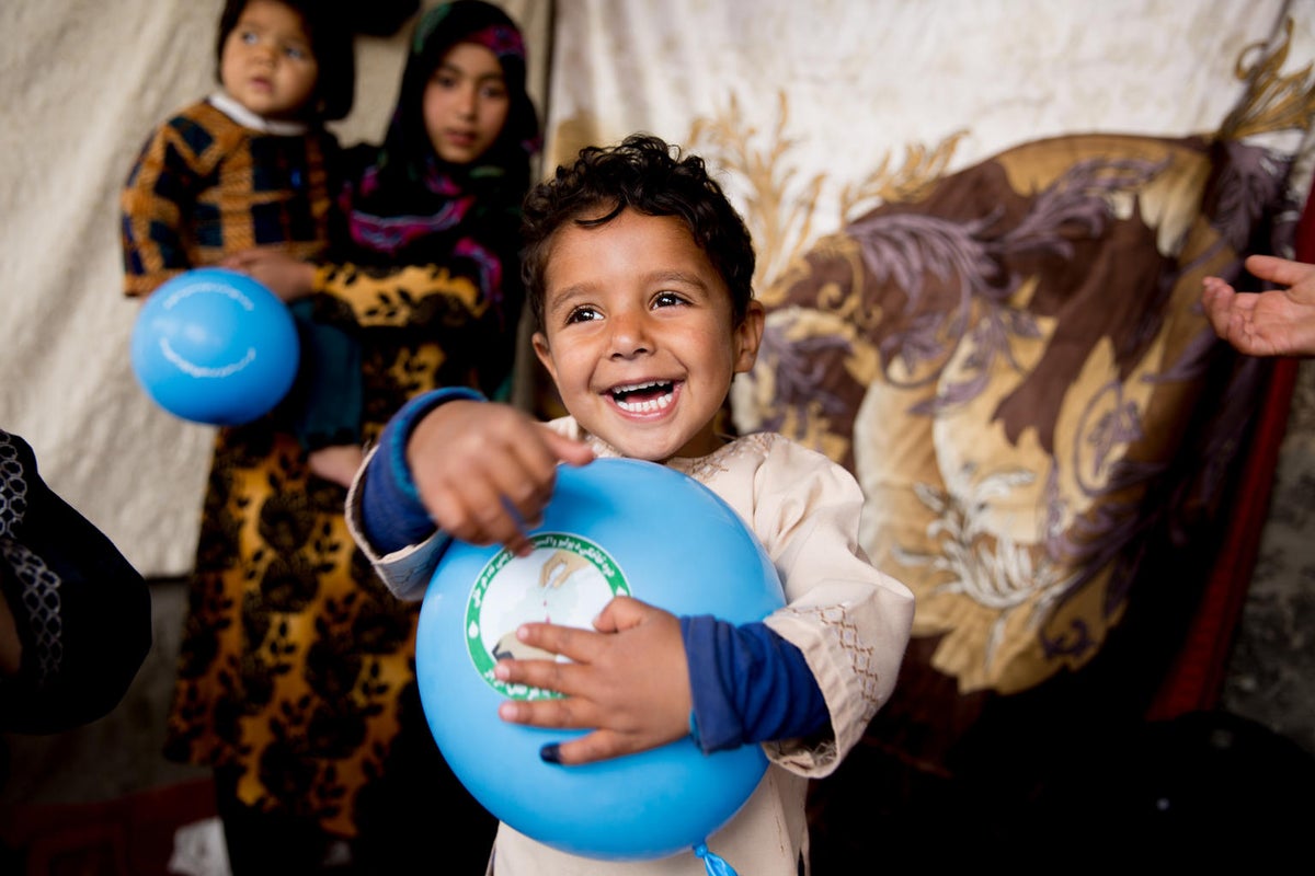 A young boy is playing with a ball and smiling.