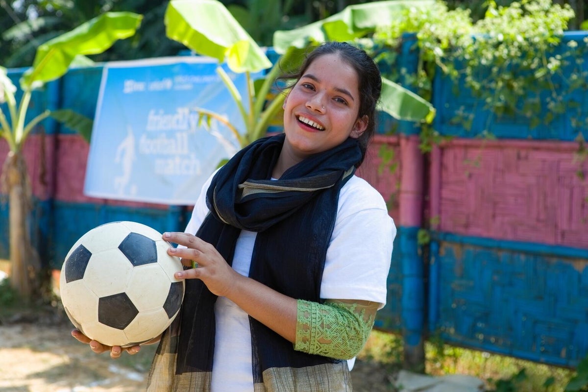 A young woman practices holds a soccer ball. 