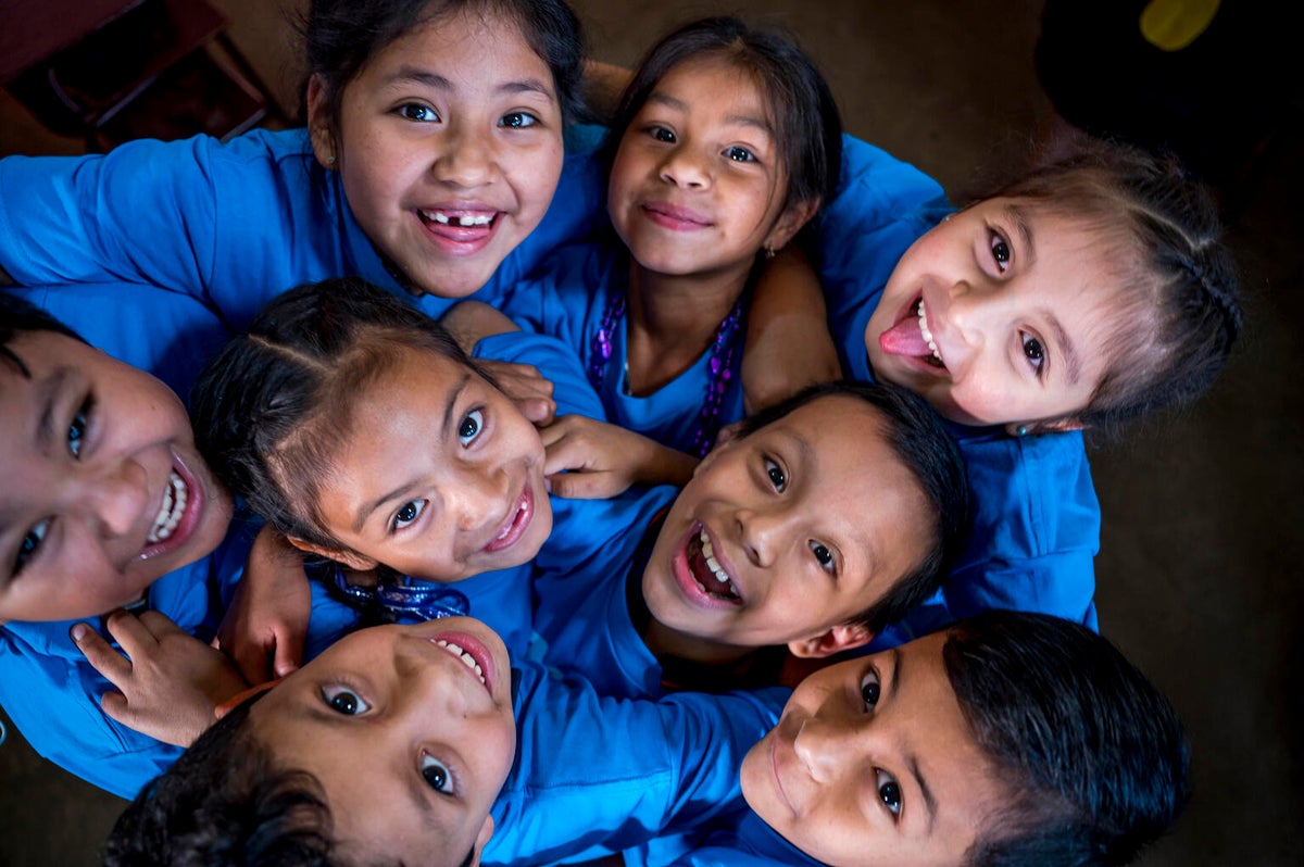 A group of children wearing blue huddle together and look up the camera. 