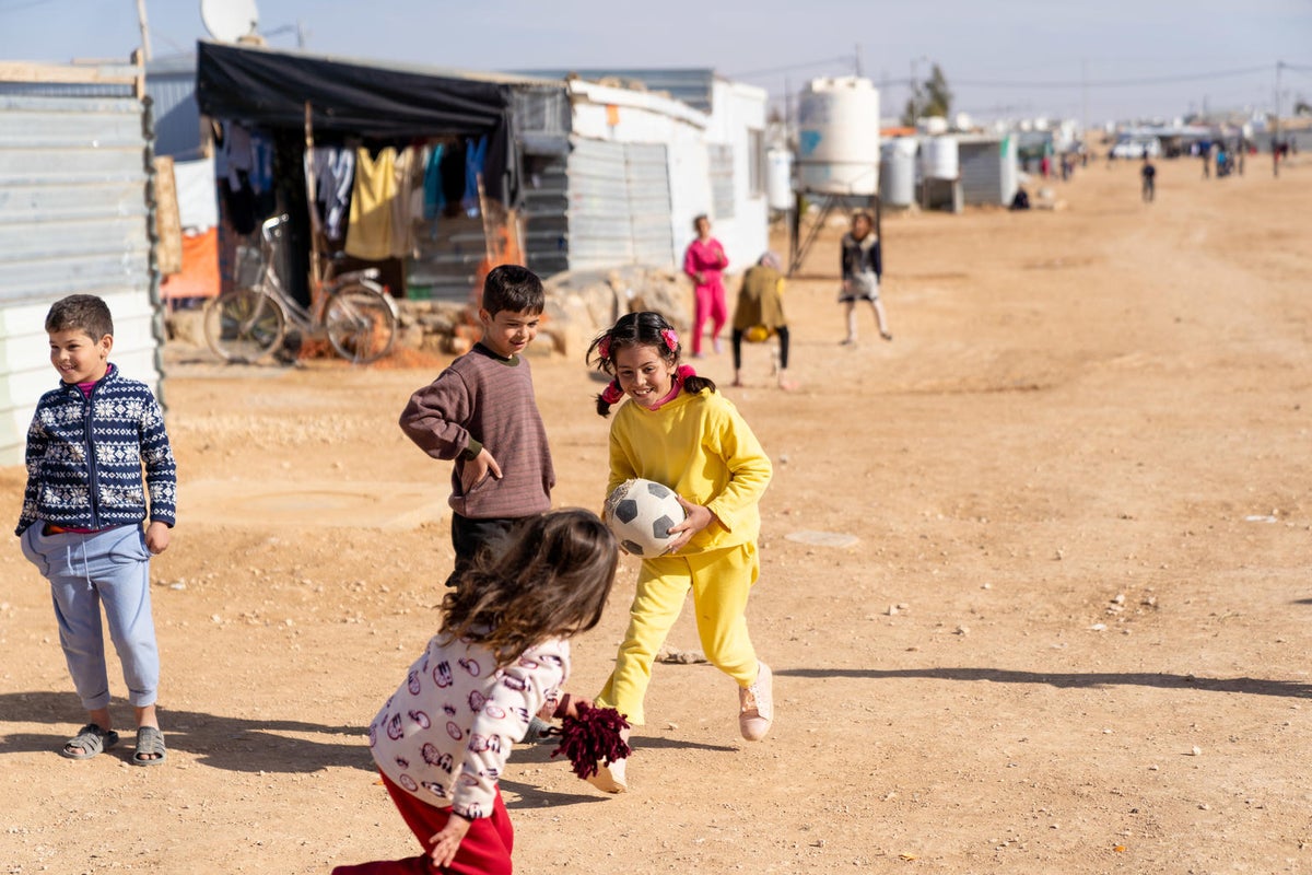 Two girls and two boys are playing soccer on a dirt road in the refugee camp.
