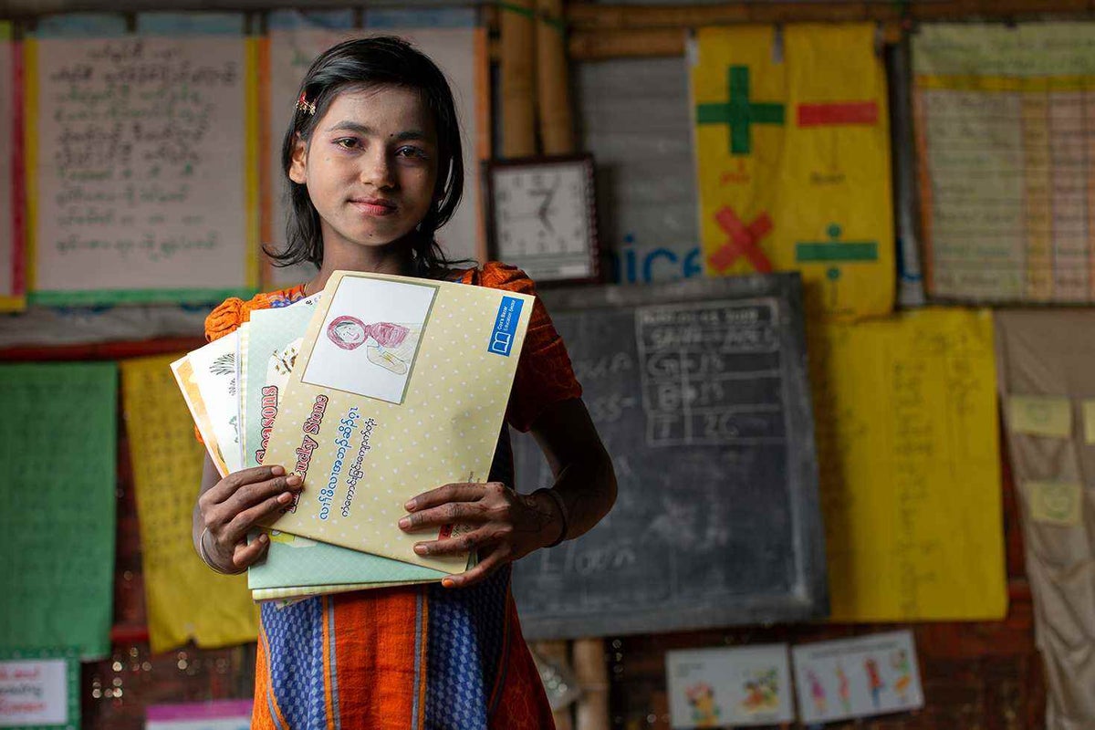 Minara, 11, stands in the UNICEF/CODEC Learning Centre she attends in Kutupalong holding a collection of Burmese and English language story books.