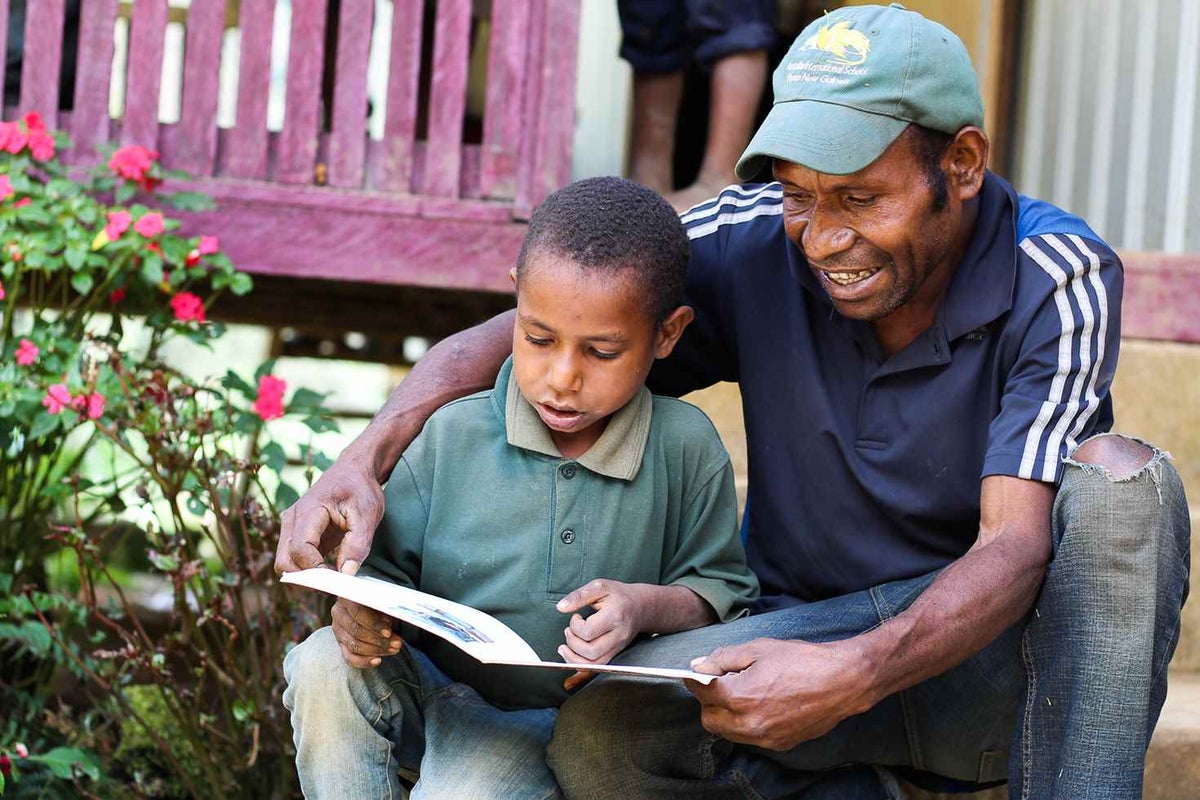 A father who participated in the program reads to his son in the mountain village of Gaglmambuno, Chimbu Province.