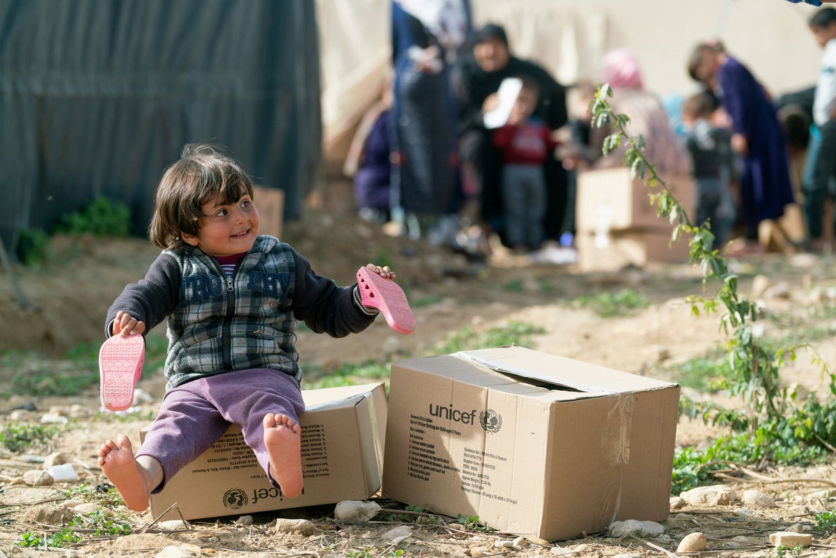 A young girl sitting on a UNICEF box full of winter clothes
