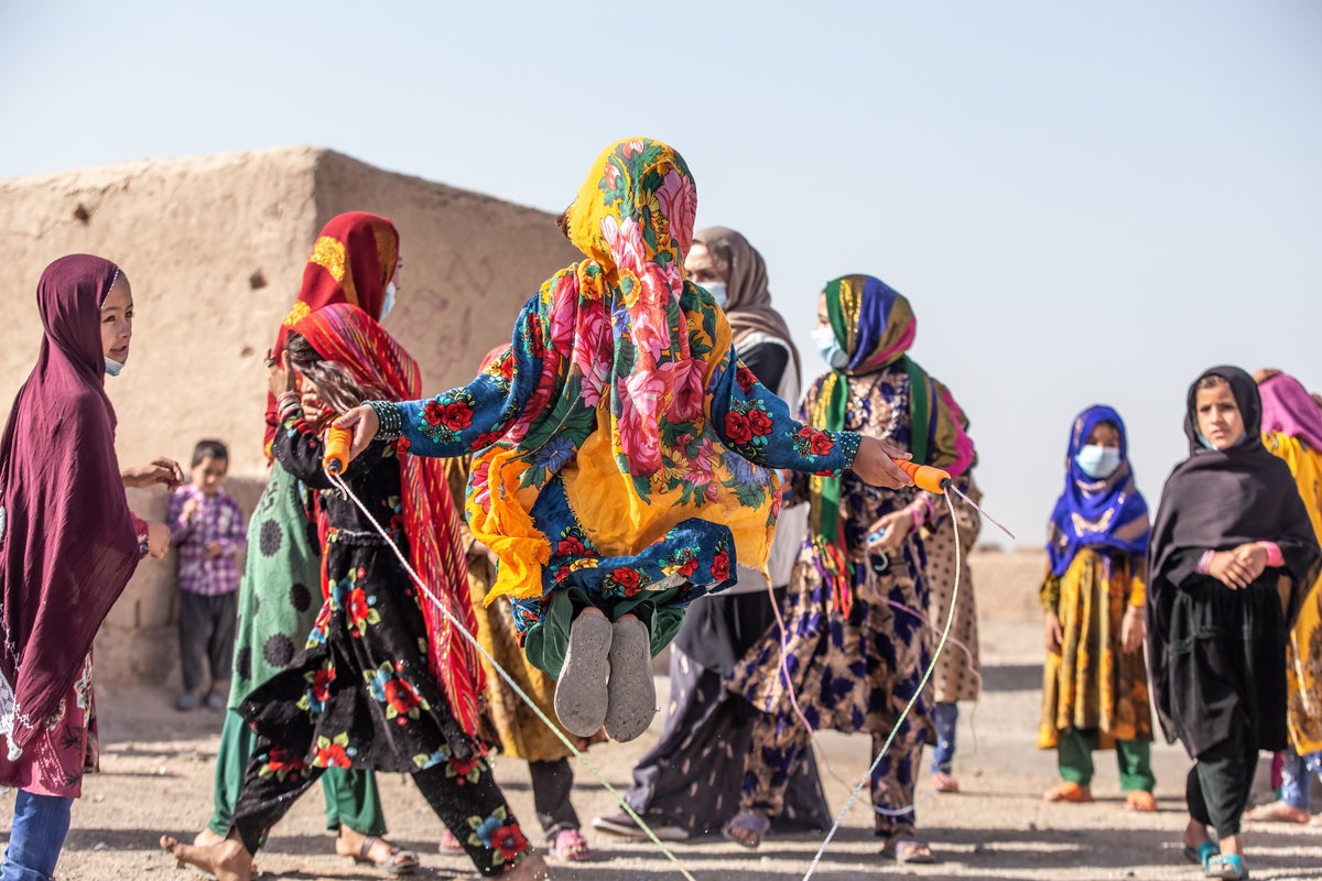 Children play skipping rope, wearing brightly coloured clothes.