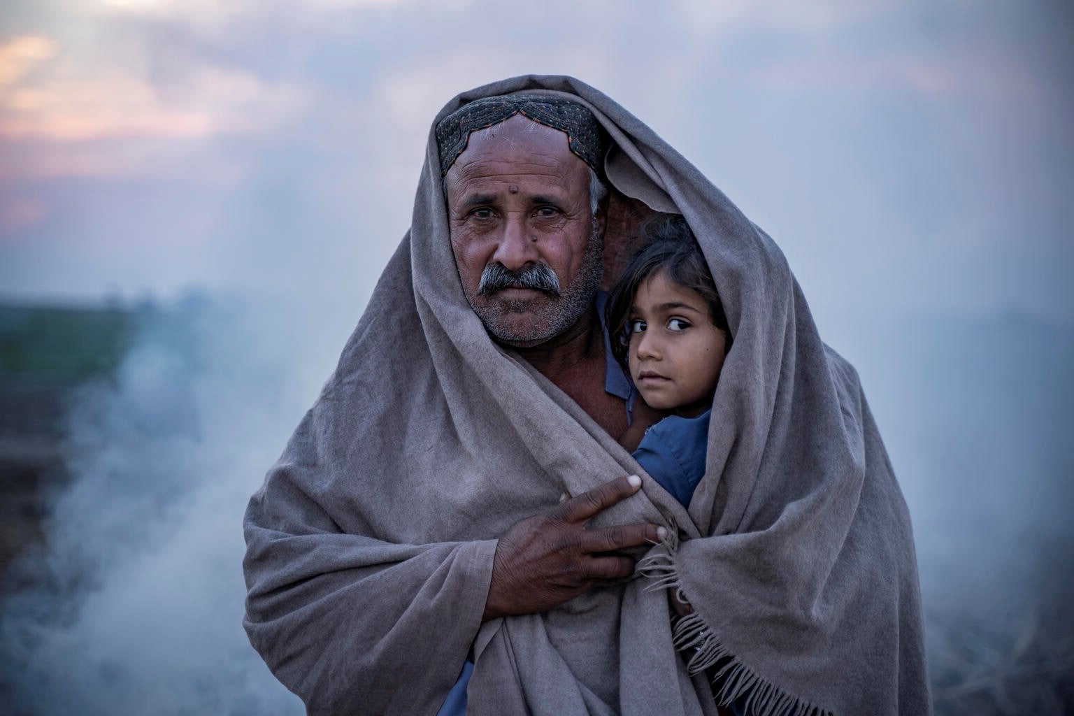 Father and child wrapped in a blanket looking at the camera