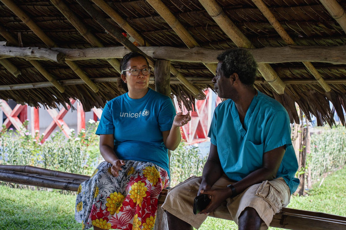 A woman speaks with a health care worker under a wooden covering.