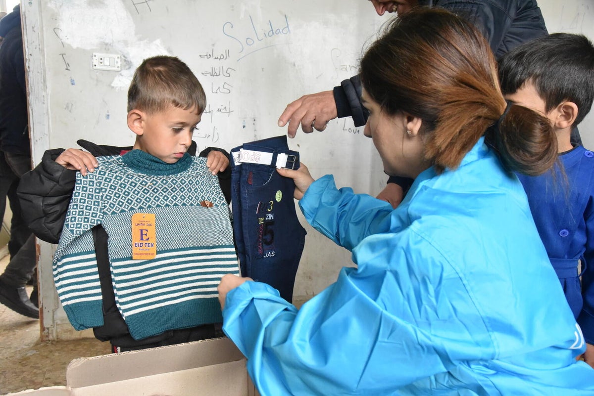 A UNICEF staff member gives a Syrian boy a jumper and a pair of pants as part of a warm clothing kit 