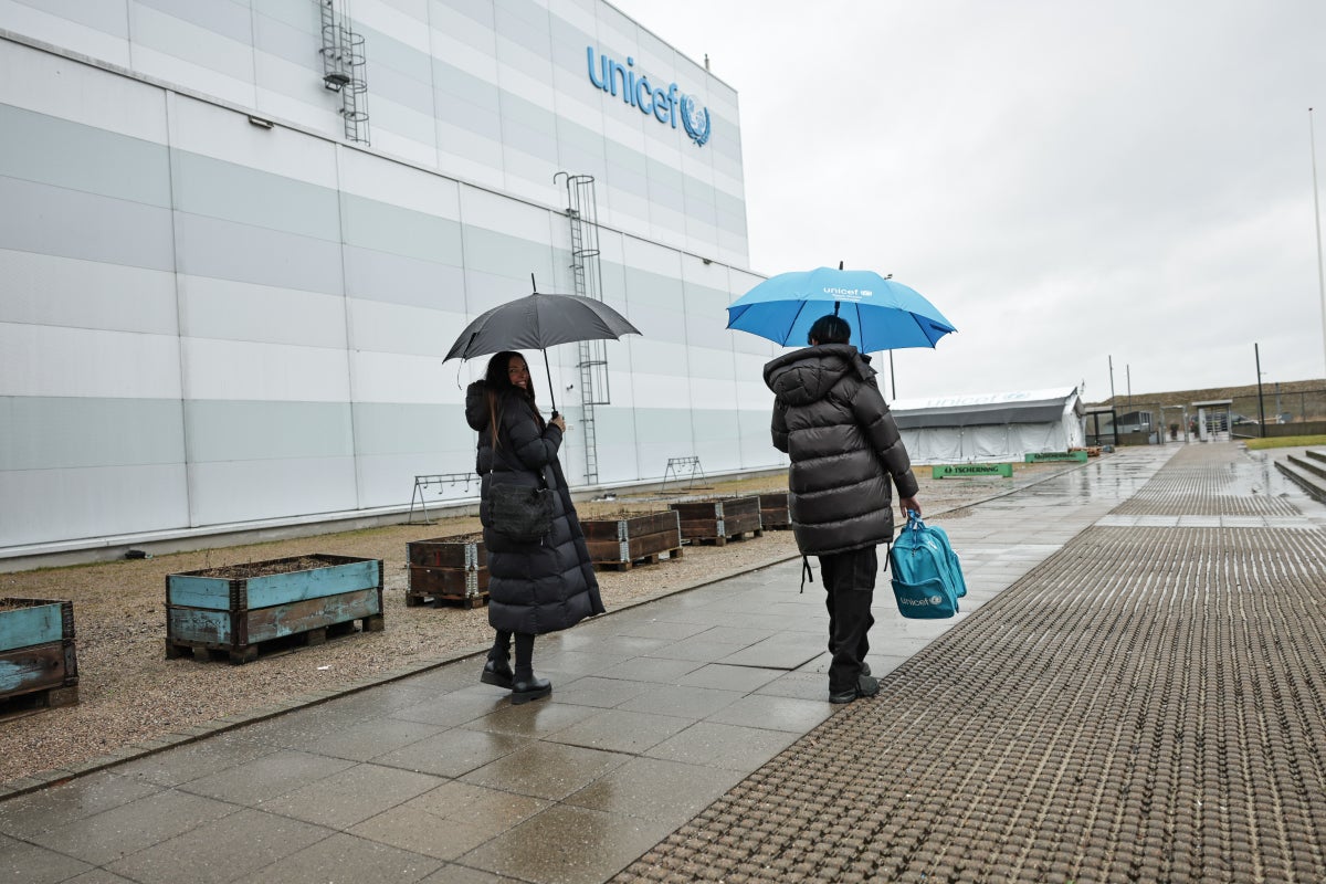 A mother and son carrying umbrellas standing outside a warehouse.