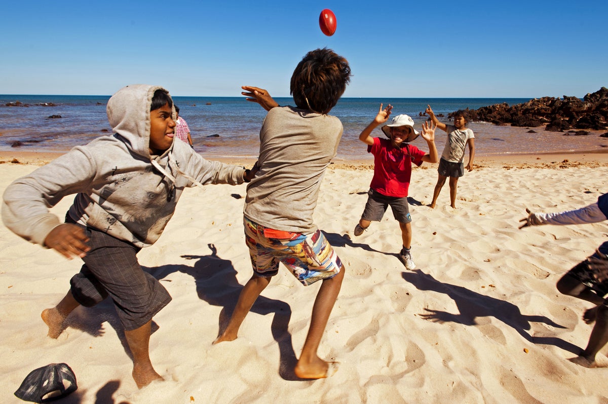 Australian children playing football on a beach.