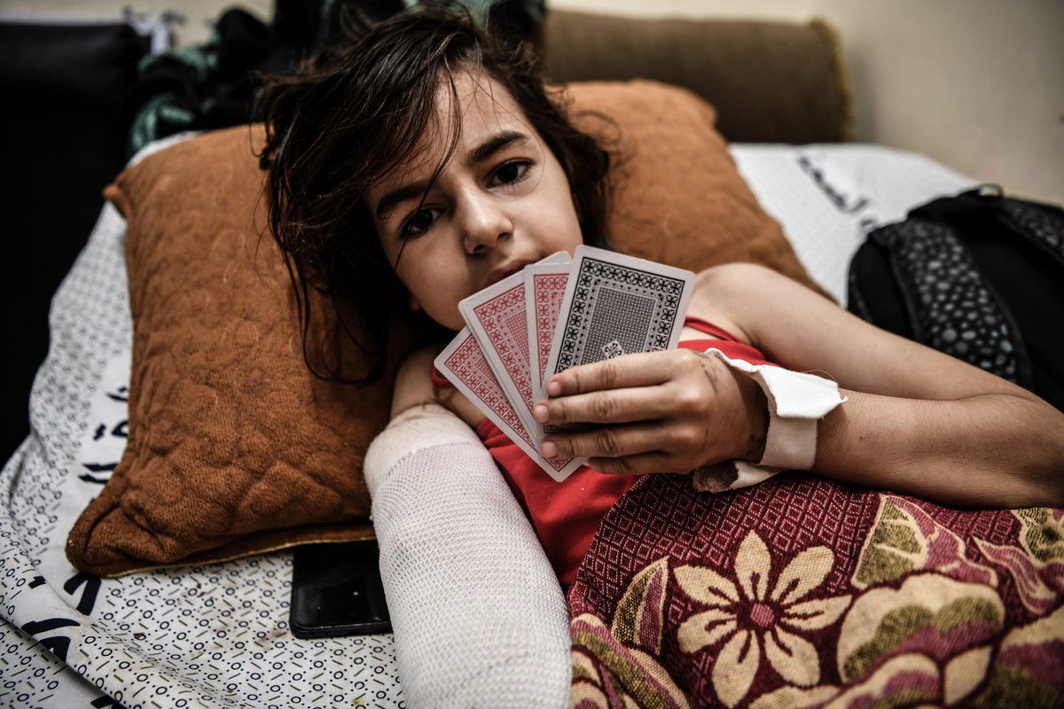 Shaimaa, an 8-year-old from Gaza City who lost her foot and her hand after her neighbour's house was shelled, holds up some playing cards while lying in a hospital bed.