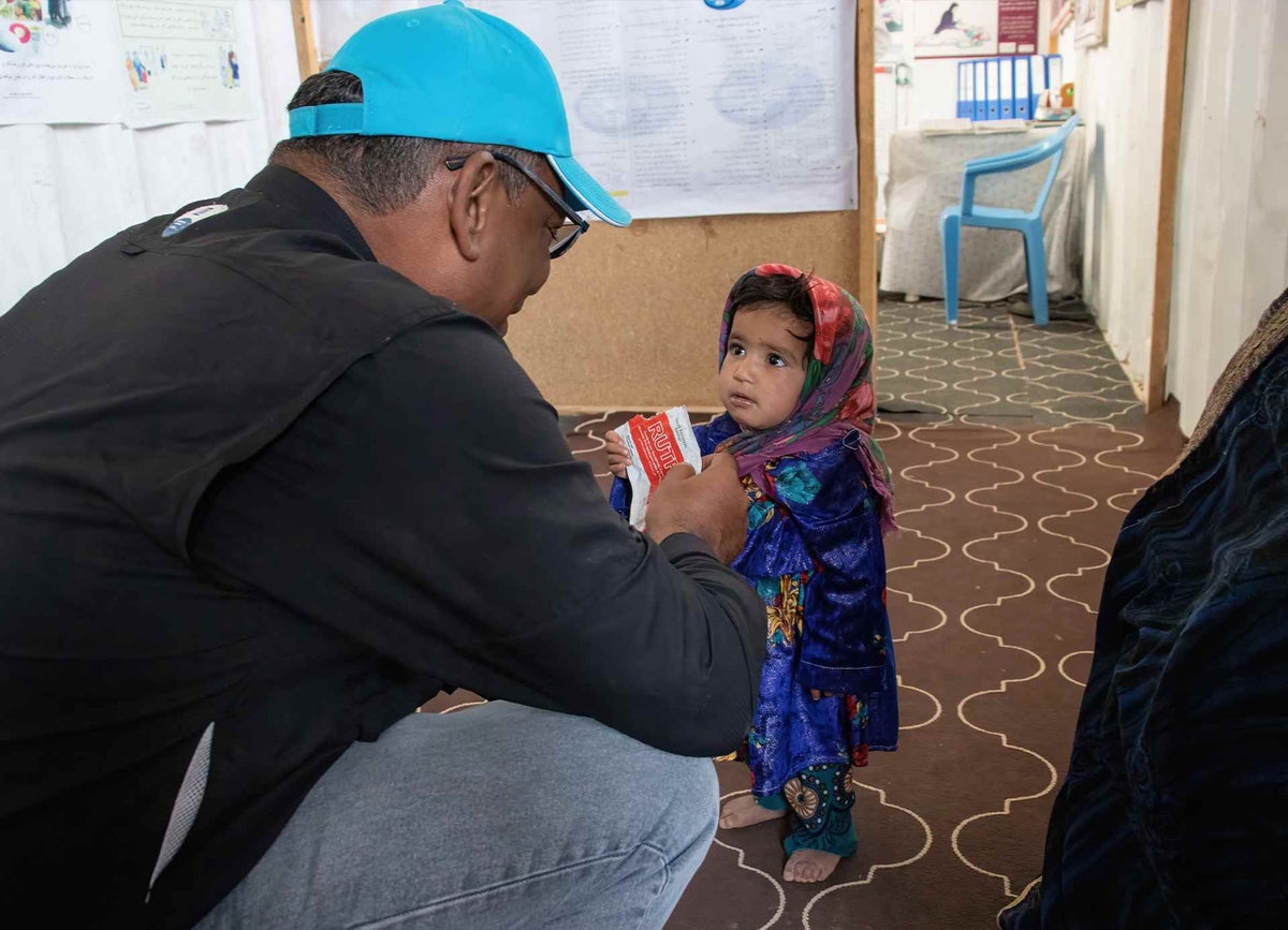 A man provides therapeutic food from a sachet to a toddler.