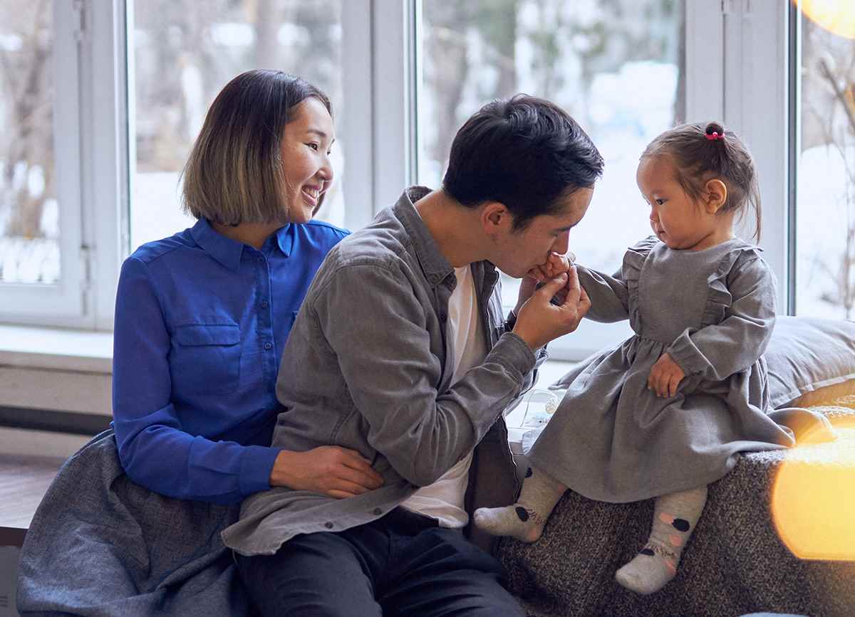 Daniyar kisses his two-year-old daughter Liya's hand while his wife sits to his left in Kazakhstan.