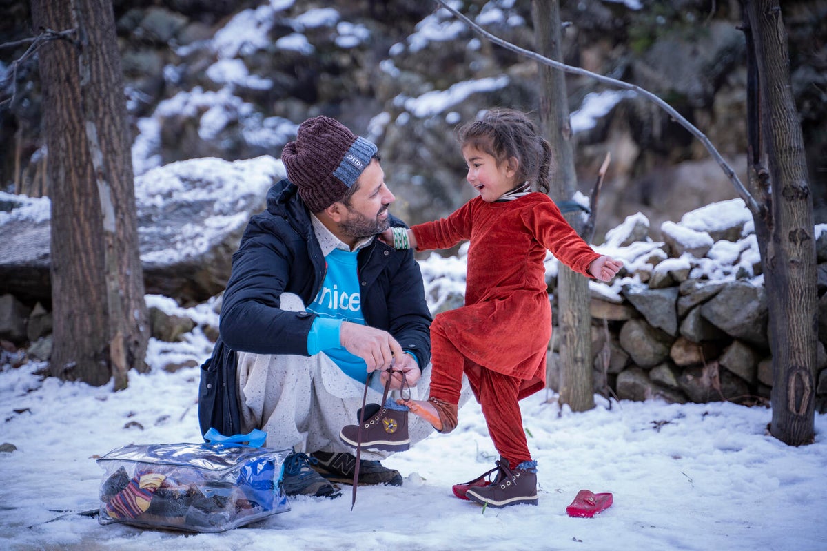 A UNICEF Pakistan staff member helps a three-year-old child put on shoes 
