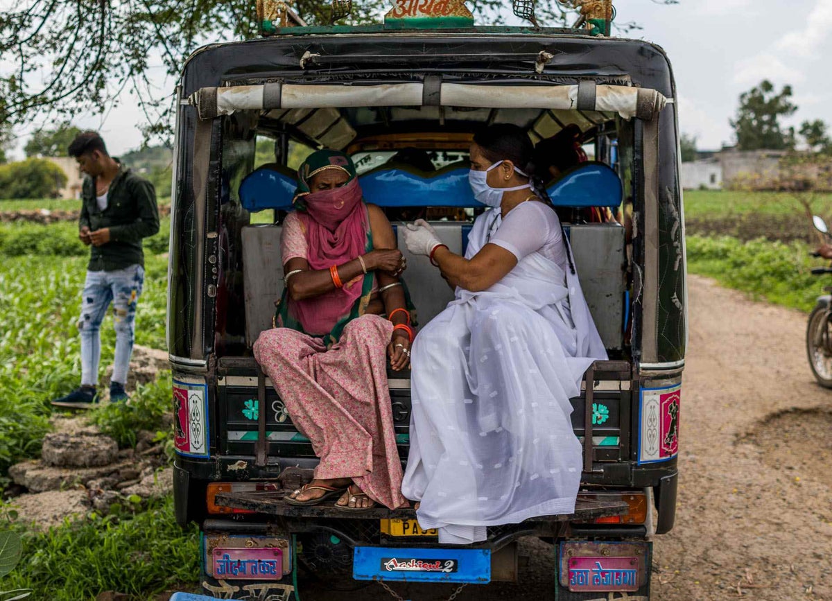 A woman receives a COVID-19 vaccination by a health worker in an open field in India.