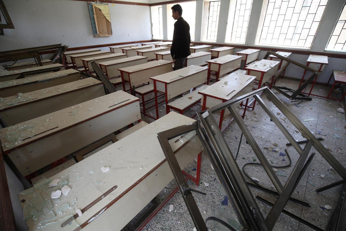 A young man is along in a classroom. There's debris as if it has been bombarded.